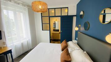 Une chambre d’hôtel avec un grand lit, un bureau, une chaise, une fenêtre avec des rideaux, un mur d’accent bleu et un luminaire suspendu.