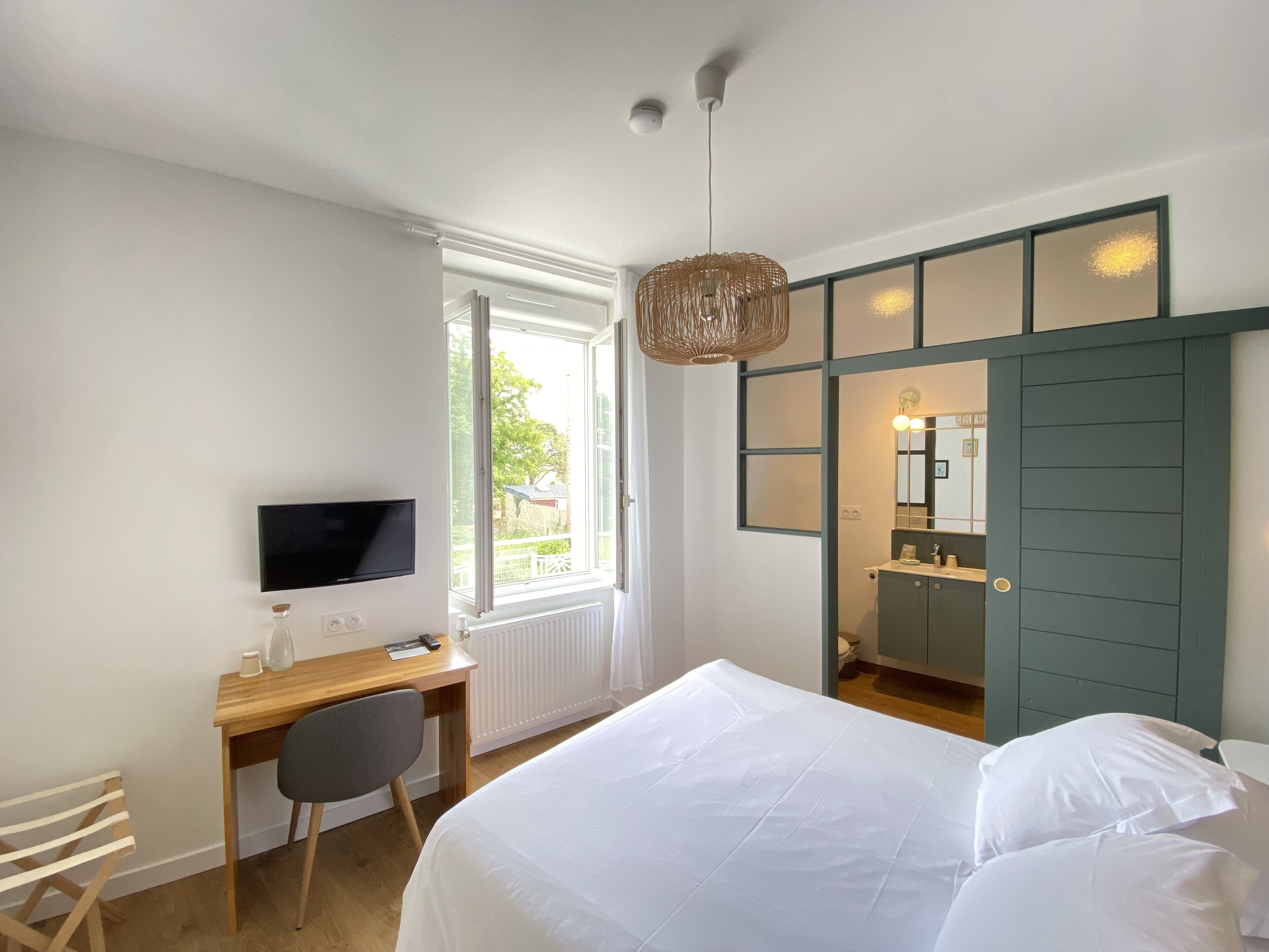 Quarto com cama, escrivaninha com computador, cadeira, televisão e janela com vista para o exterior.