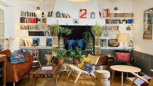 A cozy living room with a fireplace, bookshelves, comfortable seating, and a variety of plants. - Hôtel Saint-Michel (Dinard)