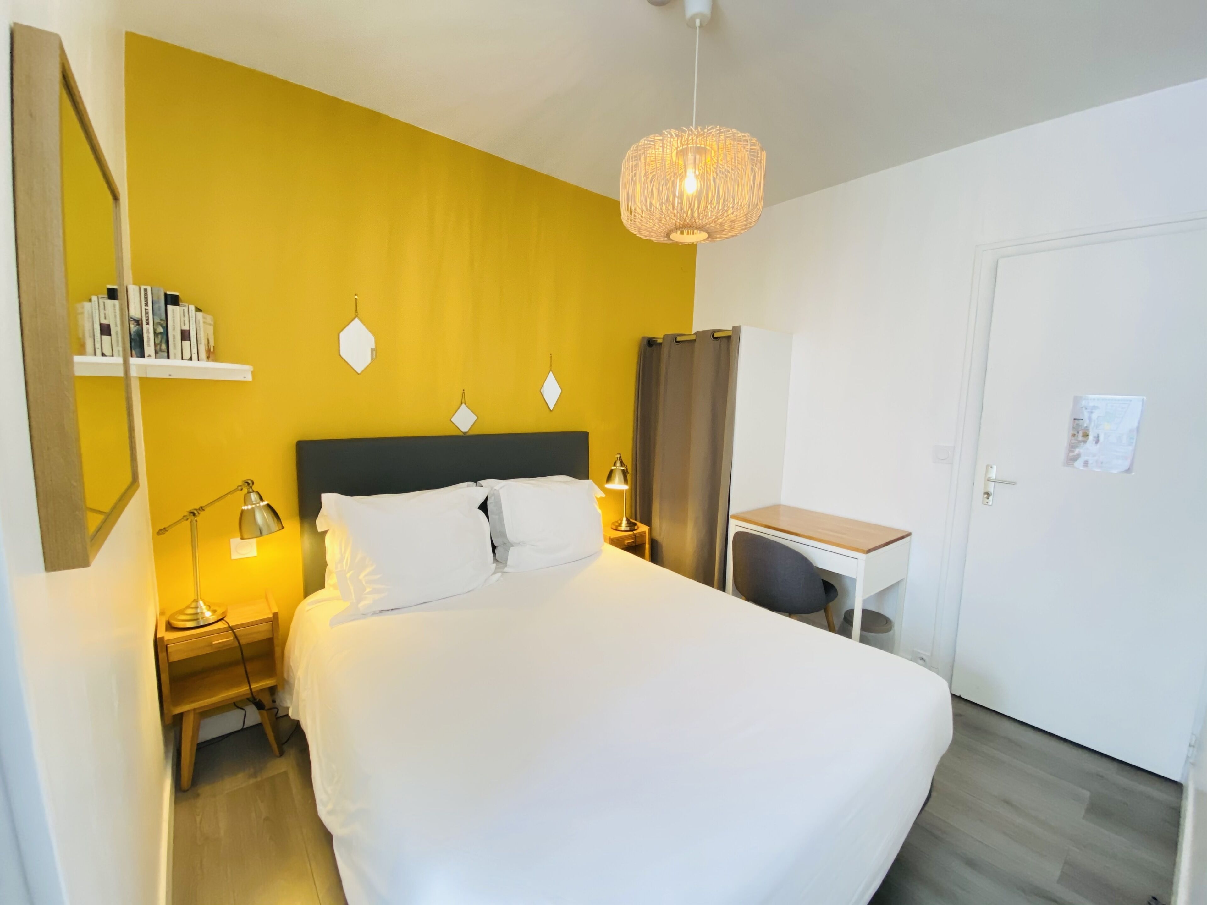 A hotel room with a bed, bedside tables, a desk, and a hanging light fixture.