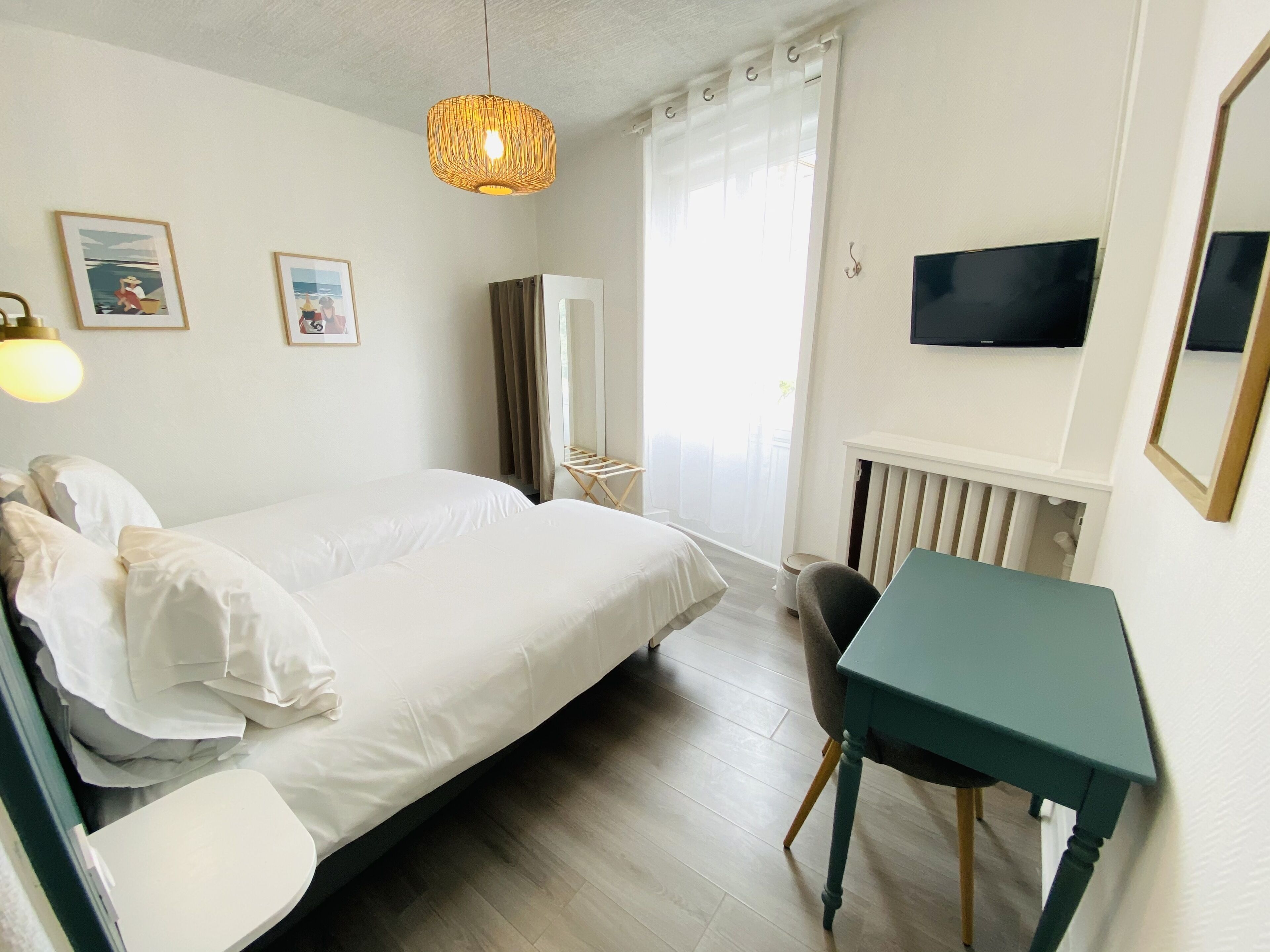 A hotel room with a bed, a desk, a chair, a television, and a radiator.