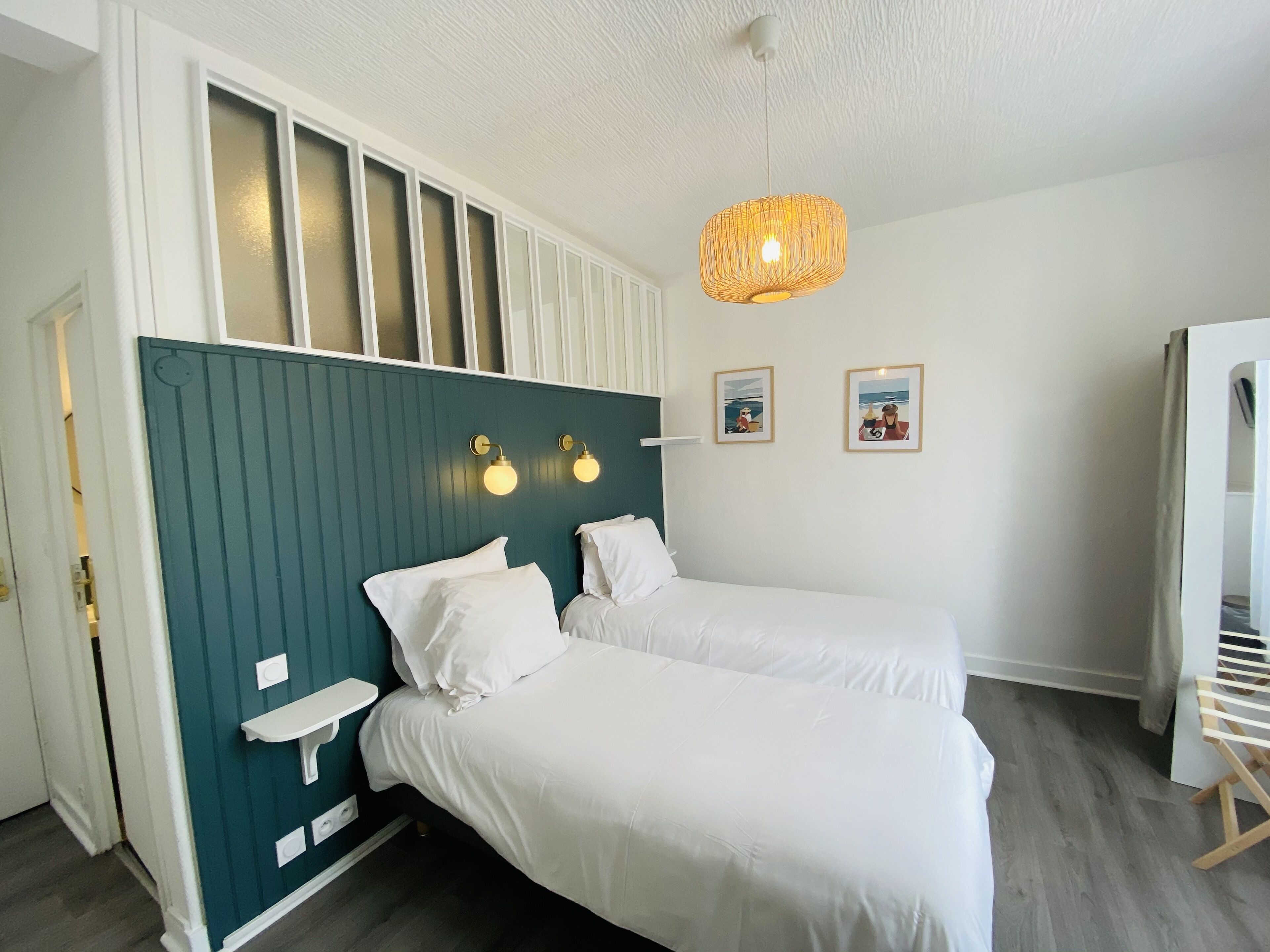 Une chambre avec deux lits, un mur d’accent de couleur turquoise et un luminaire suspendu.