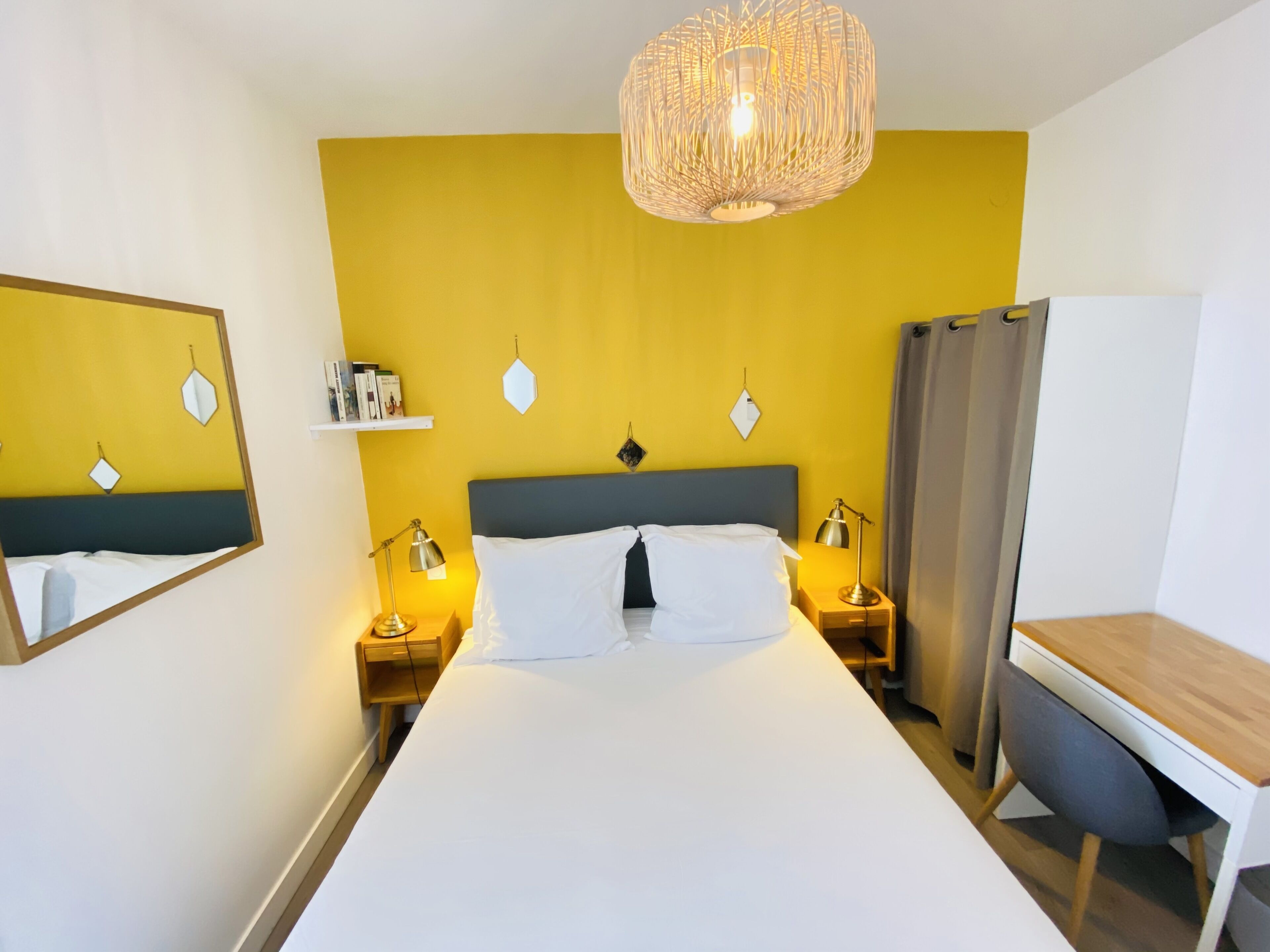 Una habitación de hotel con cama, lámparas de noche, escritorio y una lámpara colgante.