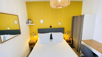 Una habitación de hotel con cama, lámparas de noche, escritorio y una lámpara colgante.