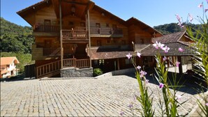 Eine Holzhütte mit Balkon, einem Steinhof und einem Berg im Hintergrund.