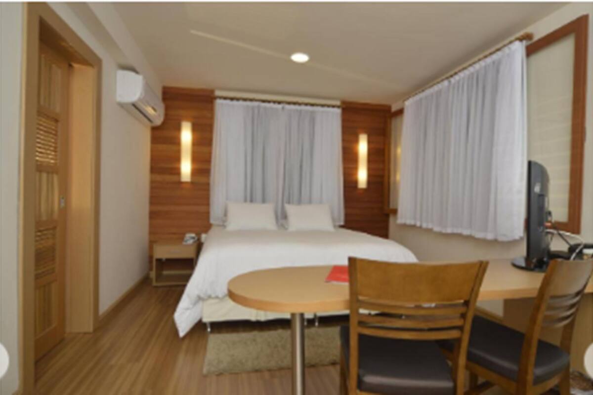 Een hotelkamer met een bed, een bureau met stoel, een televisie en een raam met gordijnen.