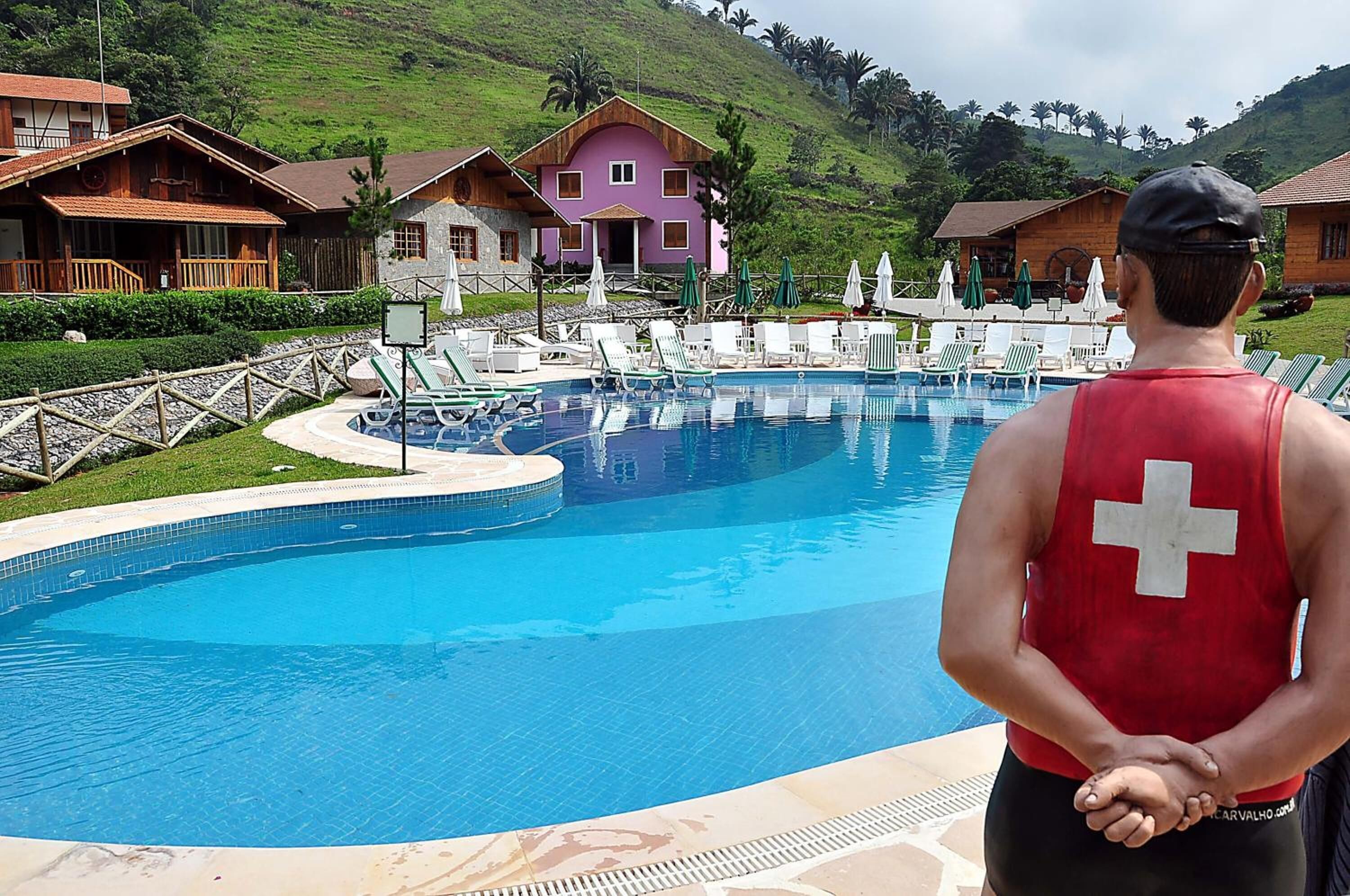 Una piscina con lettini e ombrelloni, circondata da case con uno sfondo collinare.