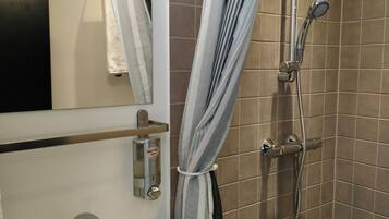Un baño con un lavabo blanco, un espejo, una ducha con cabezal de ducha manual y cortinas a rayas.