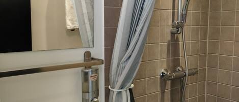 A bathroom with a white sink, a mirror, a shower with a handheld showerhead, and striped curtains.