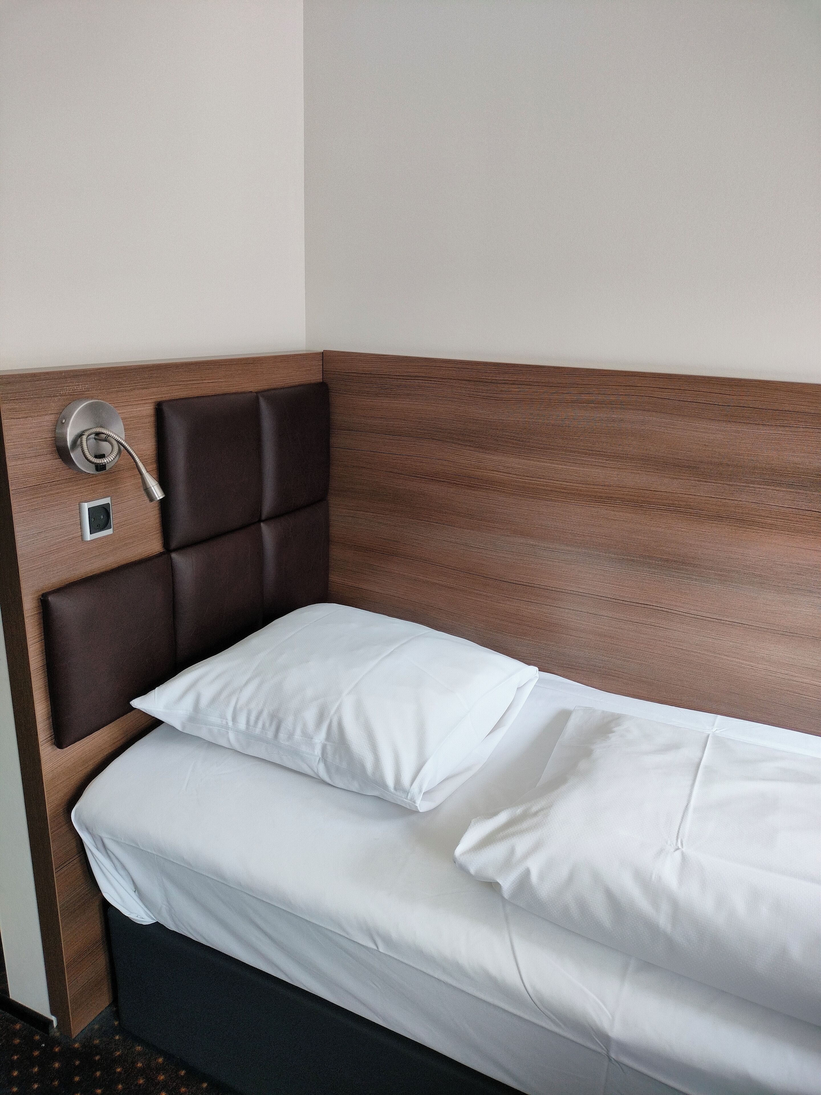 Un letto singolo con una testiera in legno e un telefono incorporato.