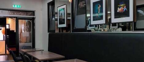 Un restaurante moderno con techos altos, asientos acolchados negros y obras de arte enmarcadas en las paredes.