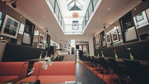 A modern hotel lobby with a high ceiling, a central chandelier, and a seating area with orange couches. - Dancenter Hotel Jomfru Ane (Aalborg)