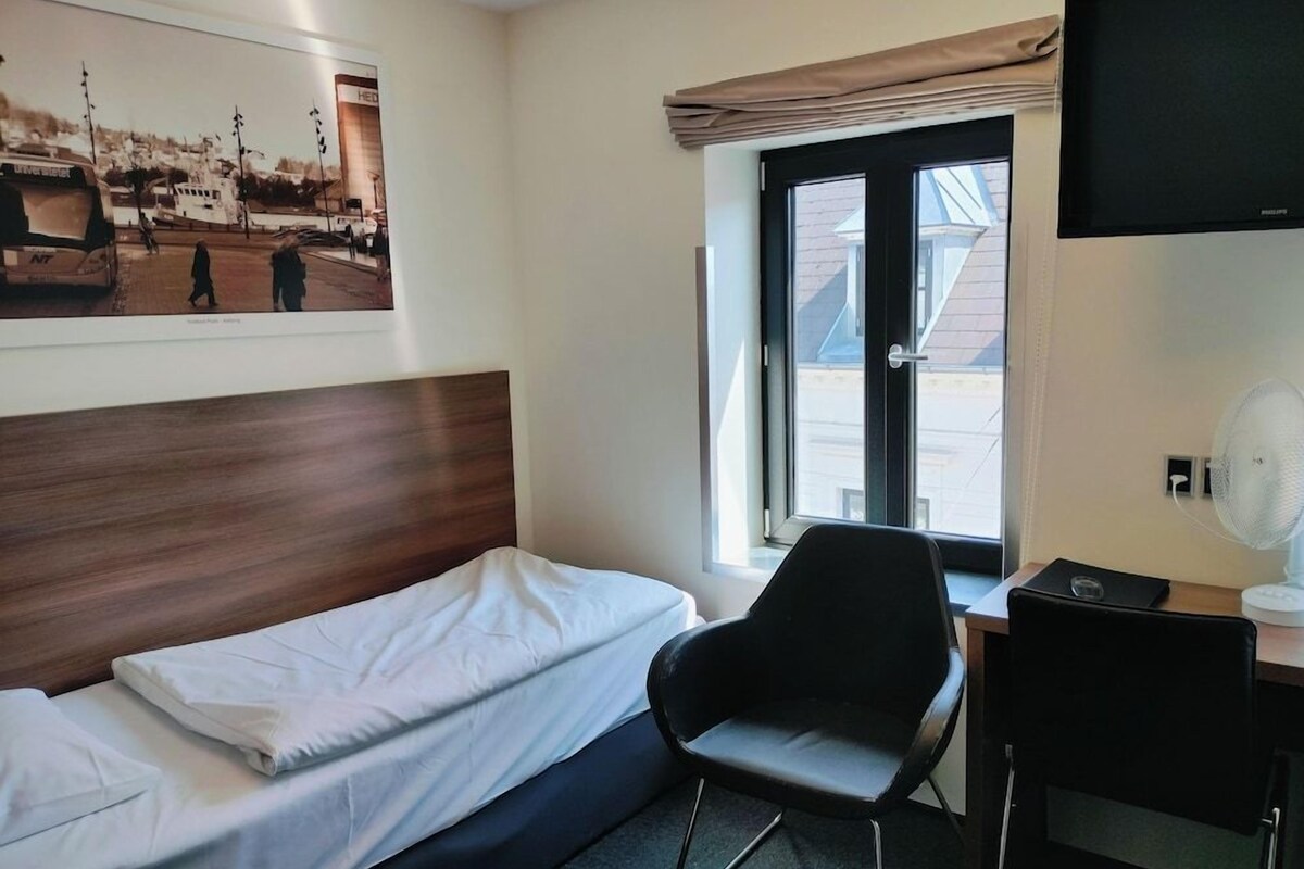 A hotel room with a bed, a desk, a chair, a television, and a window with a view of buildings.