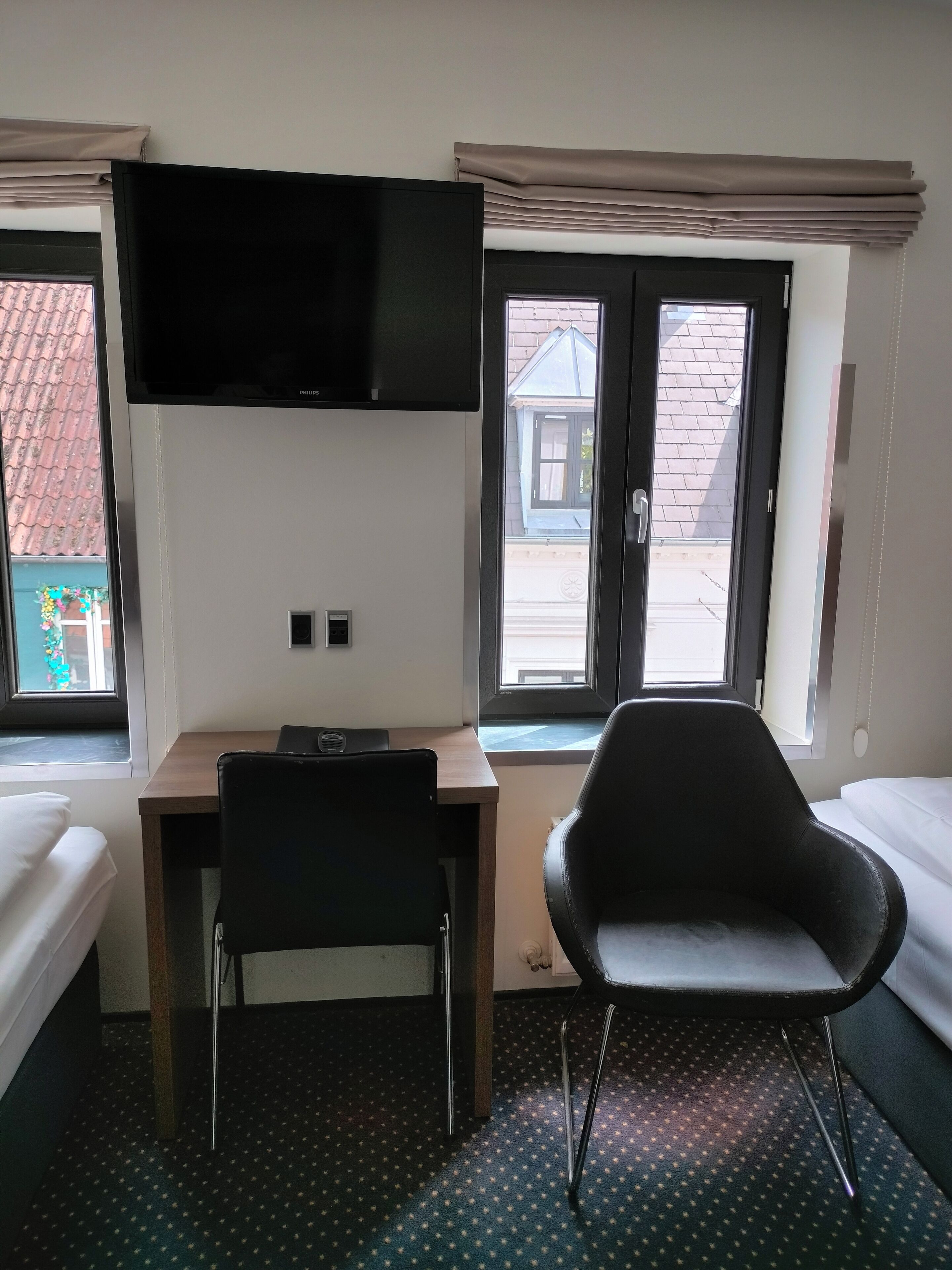 Habitación de hotel con cama, escritorio, silla, televisión y dos ventanas.