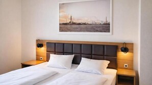 A double bed with a padded headboard, two bedside tables, and a framed cityscape picture above the bed. - Dancenter Hotel Jomfru Ane (Aalborg)