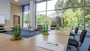 Un salón de conferencias con ventanas amplias, mesas con sillas y botellas de agua sobre posavasos.
