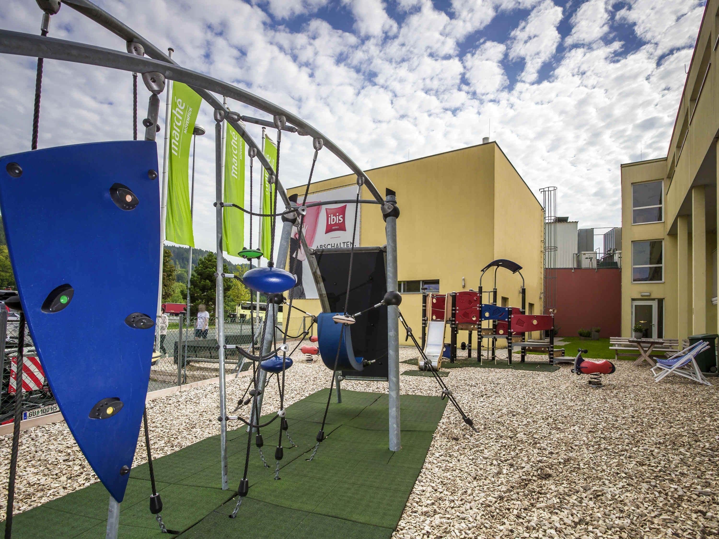 Un patio de recreo al aire libre con estructuras para escalar, un edificio amarillo al fondo y suelo de grava.