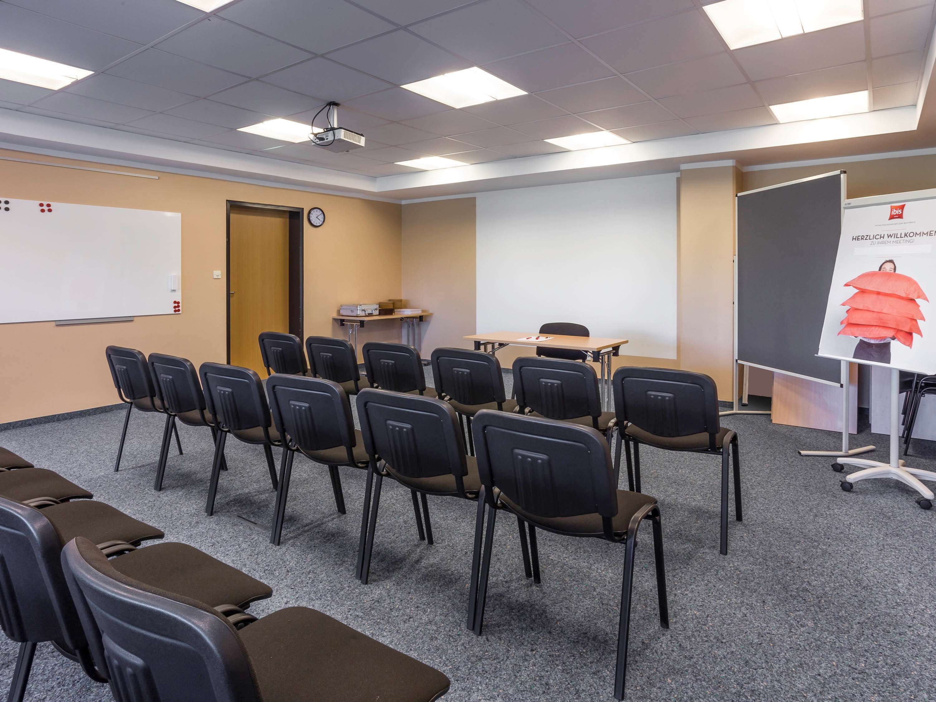 Una sala conferenze con file di sedie, una lavagna, un proiettore e uno schermo per presentazioni.