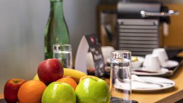 A breakfast setting with fruits, a coffee machine, and a salt shaker on a table.