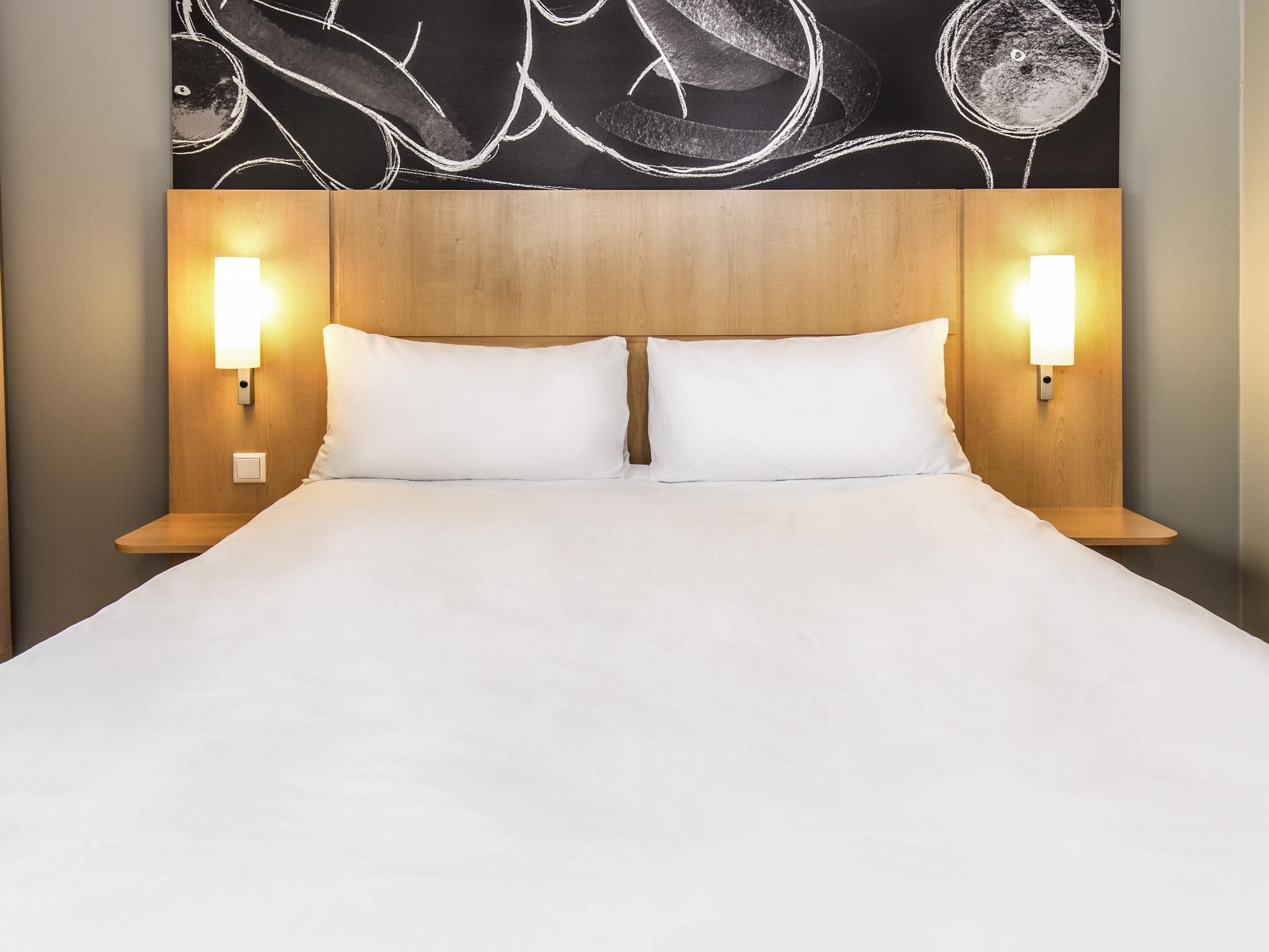 A hotel room with a wooden headboard, two bedside lamps, and a white bedspread.