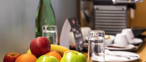 A breakfast setting with fruits, a water glass, and a coffee machine.