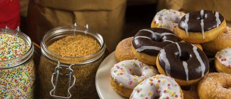 A variety of donuts on a plate, with sugar and sprinkles in jars.