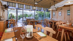 Un restaurante con mesas y sillas de madera, ventanas amplias y vistas al exterior.