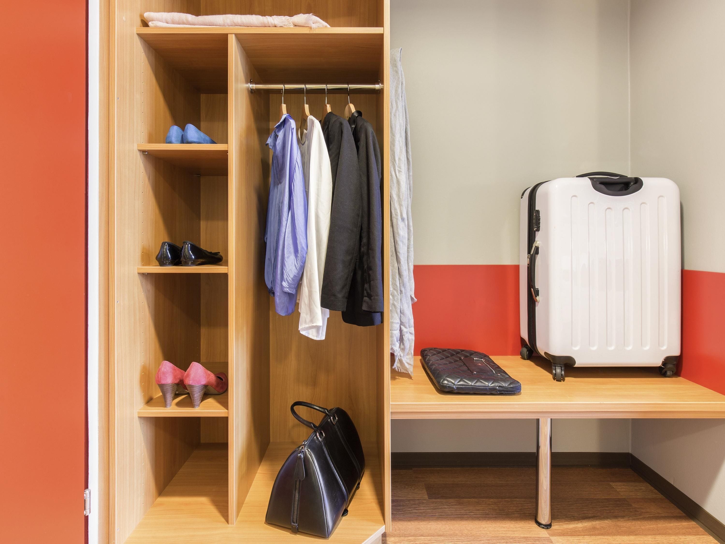 Una habitación con un armario de madera, un escritorio, una maleta y un bolso.