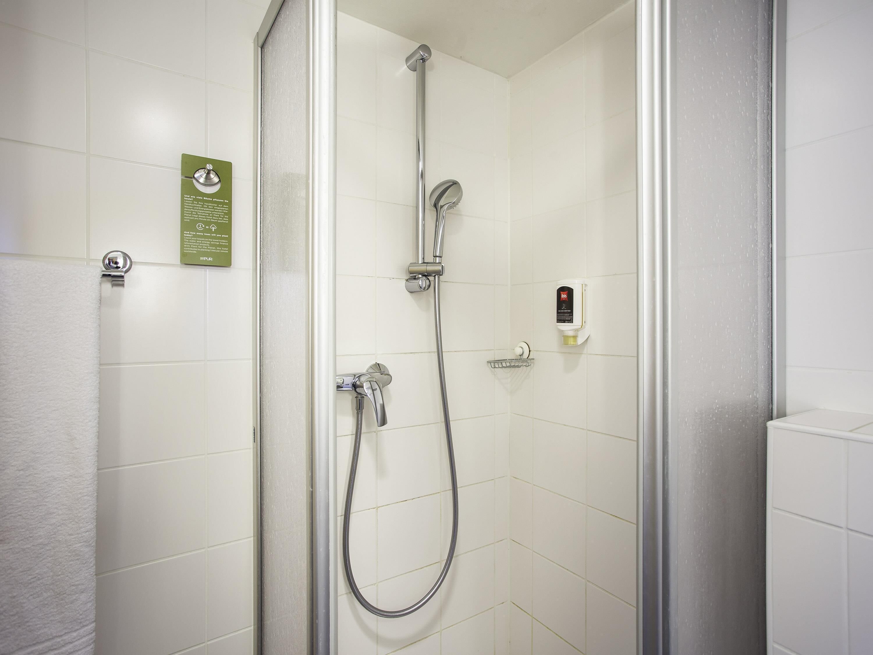 Eine Dusche mit Duschbrause, Wandarmatur und Seifenspender.