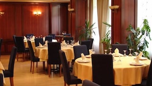 A dining area with round tables set for four, each with a white tablecloth, black chairs, and neatly arranged cutlery and napkins.