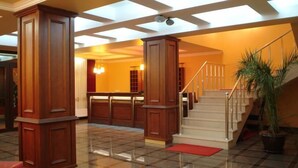 A spacious lobby with a grand staircase, wooden paneling, and a red doormat at the base.