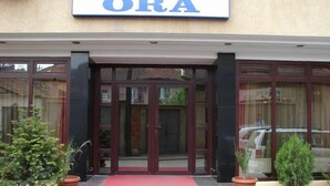 A hotel entrance with a glass door, a red carpet, and a sign above reading "ORA".