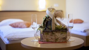 Siististi järjestetty aamiaiskori pyöreällä pöydällä, jonka päällä on kaksi viinilasia. Taustalla näkyy hotellihuone, jossa on sänky ja tyynyjä.