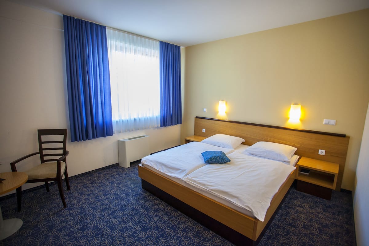 Une chambre d’hôtel avec un grand lit, deux tables de chevet, une chaise, un bureau et une fenêtre avec des rideaux.