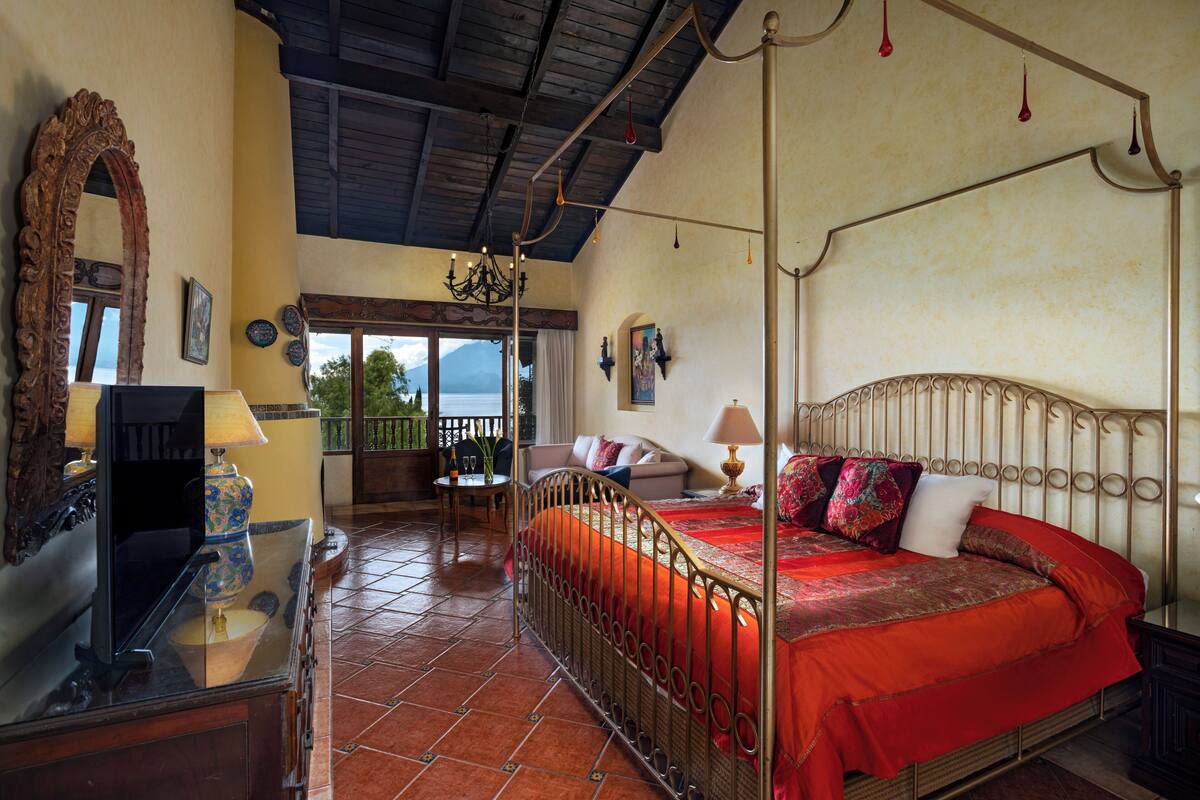 Un dormitorio amplio con cama con dosel, un espejo grande y decorativo, y vistas al exterior.