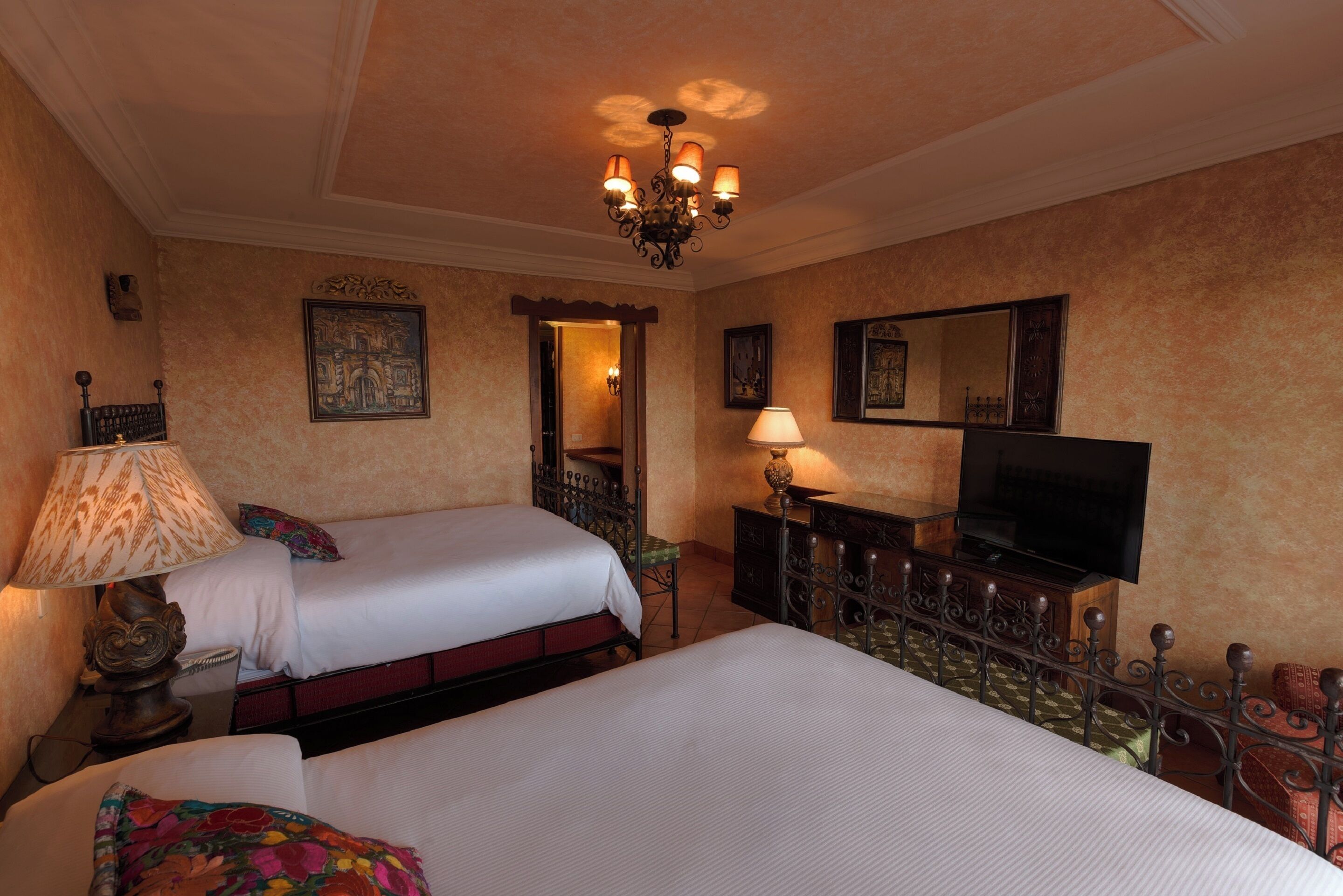 Una habitación de hotel con dos camas, televisión, candelabro y obras de arte en las paredes.