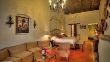 A traditional room with a four-poster bed, a sofa, a chair, and a small table with a bottle and glasses.