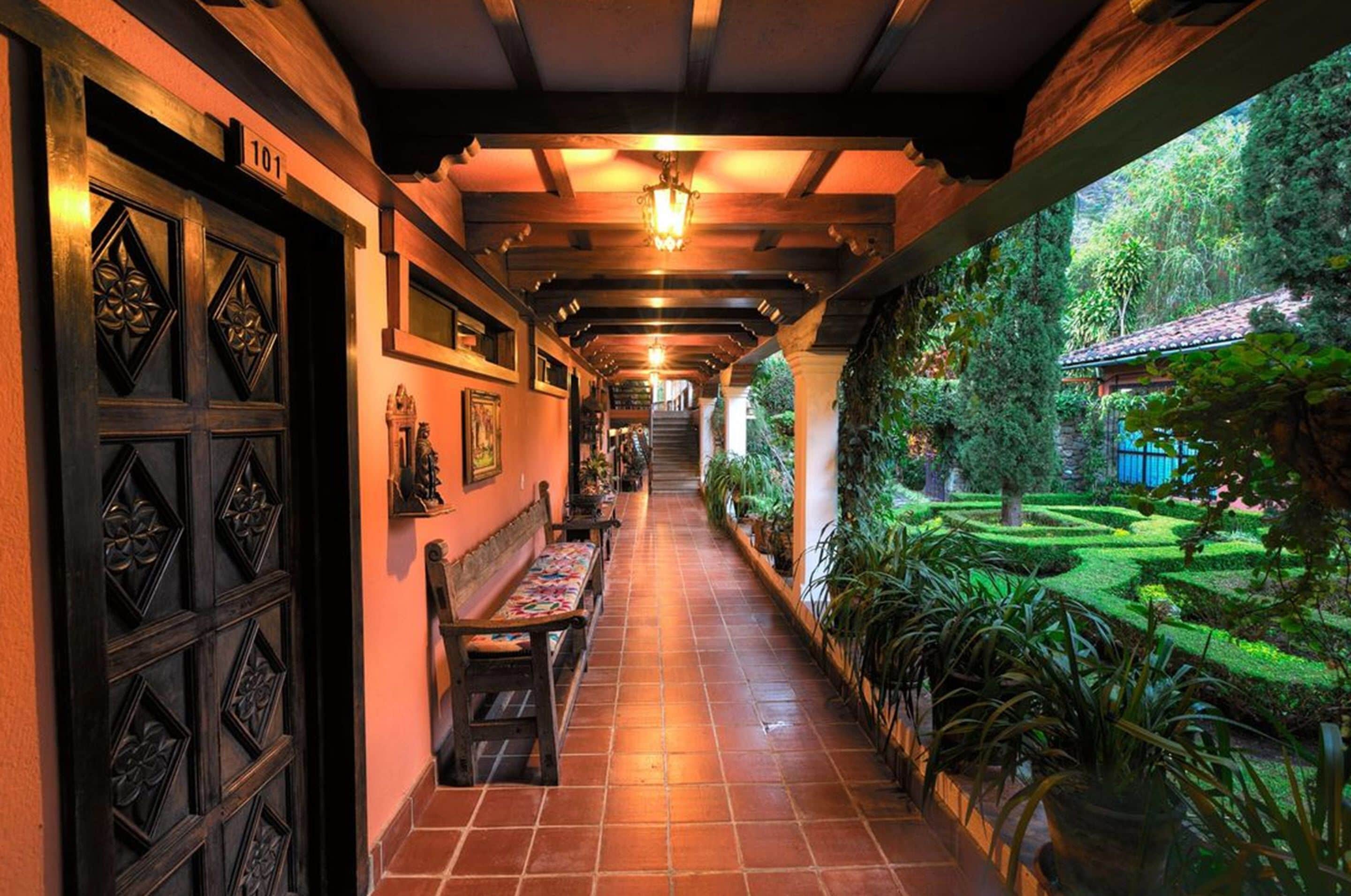 A corridor with a bench, a door with a number, and a view of a garden.