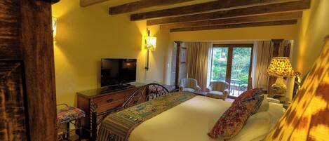 A bedroom with a large bed, a television, a wooden headboard, and a window with curtains.