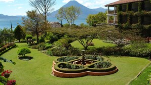 A well-maintained garden with a fountain, a mountain in the background, and a building with a balcony. - Hotel Atitlán (Panajachel)