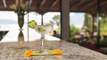 A martini glass with a lime wedge on a granite countertop, a yellow napkin, and a vase with flowers in the background.
