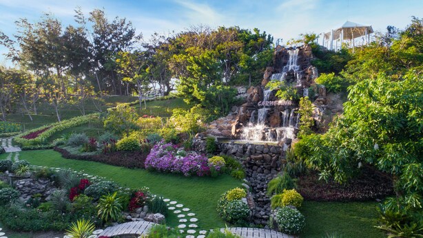 A landscaped garden with a waterfall, stone pathways, and a gazebo.