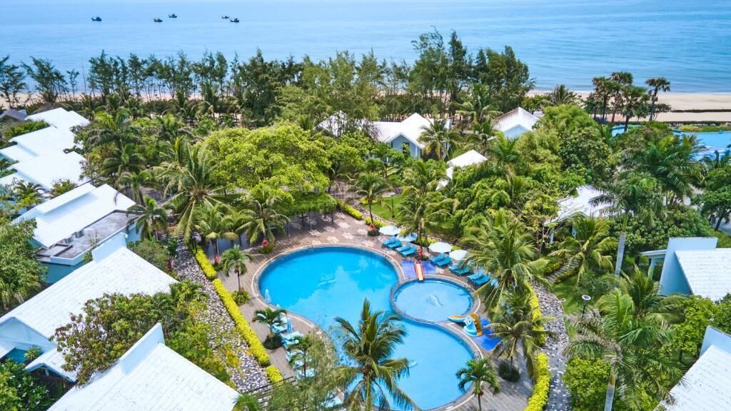 Ein Resort mit mehreren Schwimmbecken, umgeben von üppiger Vegetation und Palmen, mit Blick auf einen Strand.
