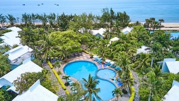 Ein Resort mit mehreren Schwimmbecken, umgeben von üppiger Vegetation und Palmen, mit Blick auf einen Strand.