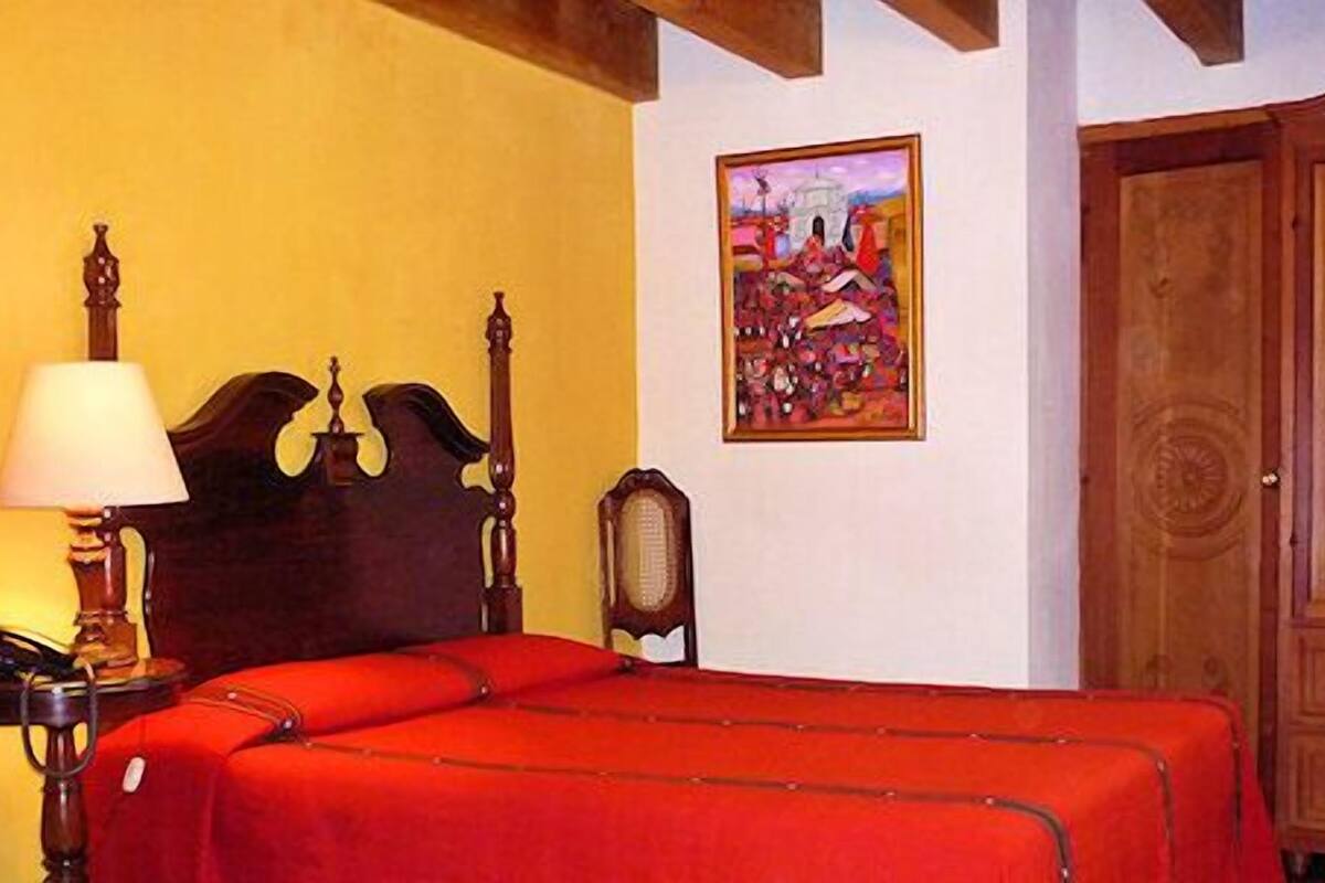 Une pièce comprenant un lit, une armoire en bois, une lampe et un tableau accroché au mur.
