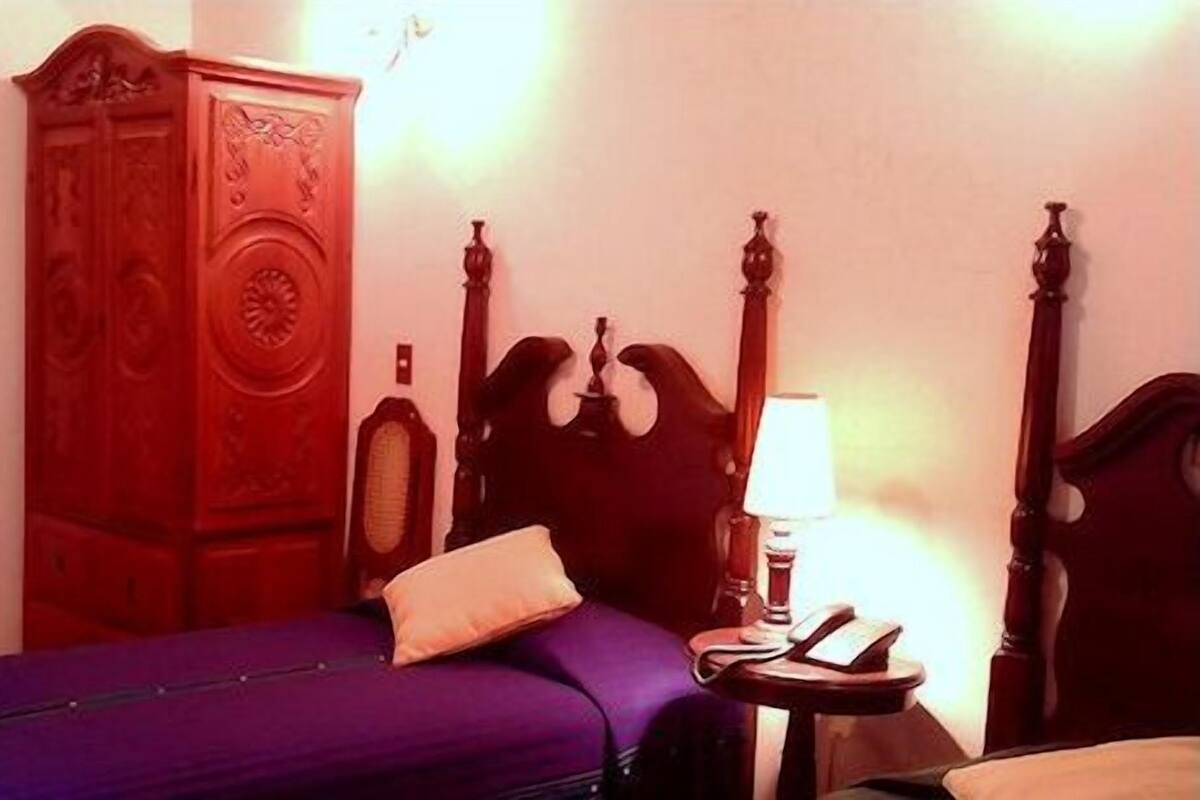 Une pièce comprenant un lit, une armoire en bois, une table de chevet avec une lampe et une porte.