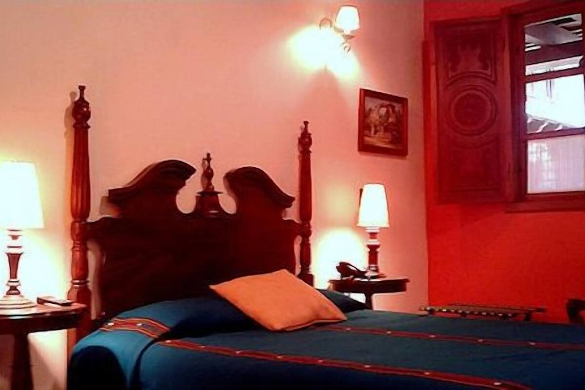 Une chambre avec un lit, deux tables de chevet, une commode, une fenêtre donnant sur un beau paysage et un tableau accroché au mur.