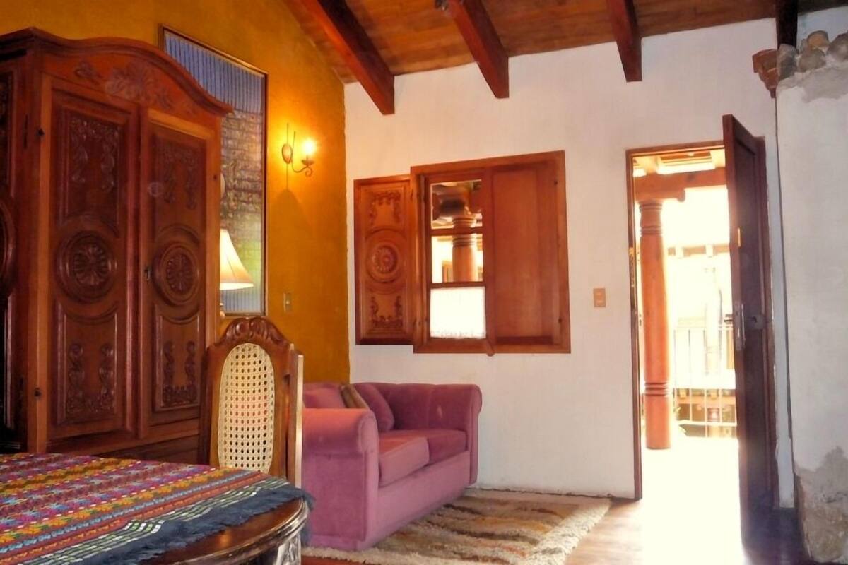 Une pièce avec un lit en bois, un canapé rose et une grande armoire en bois.