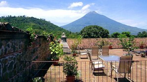 Une terrasse sur le toit offrant une vue sur un volcan, avec des murs en pierre et des plantes en pot.