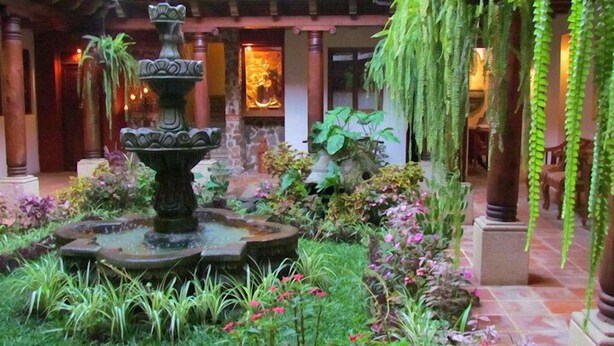 Une cour intérieure avec une fontaine centrale, entourée d’une végétation luxuriante et de plantes en fleurs.